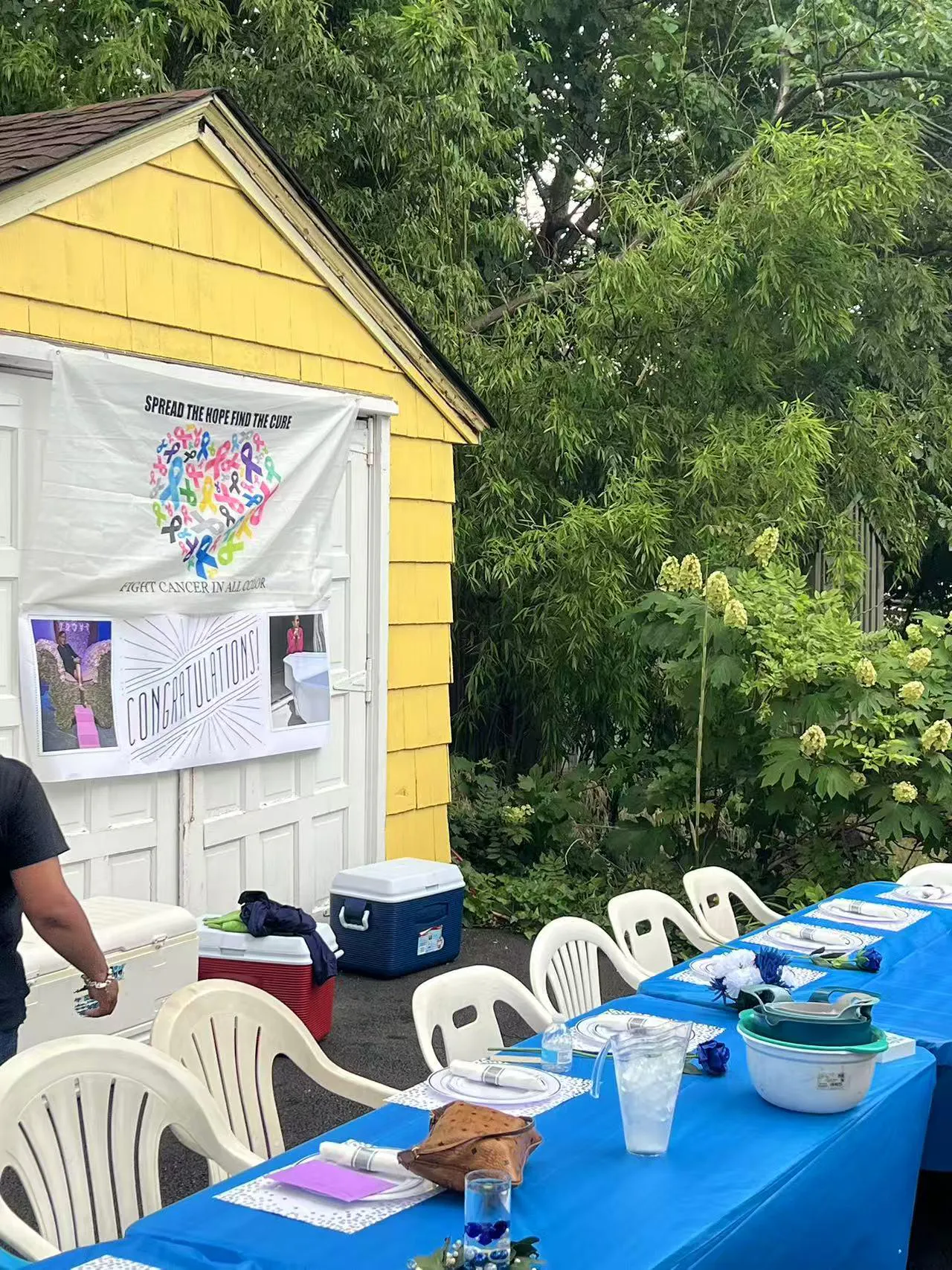 Cancer awareness banner on yellow shed at outdoor event with blue tables