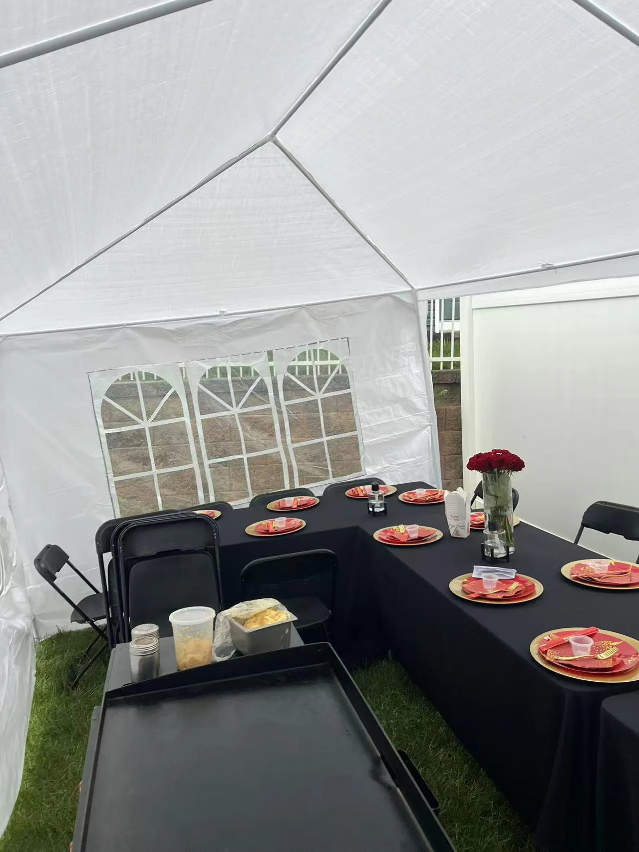 White event tent with black/red table settings, red roses, and catering griddle