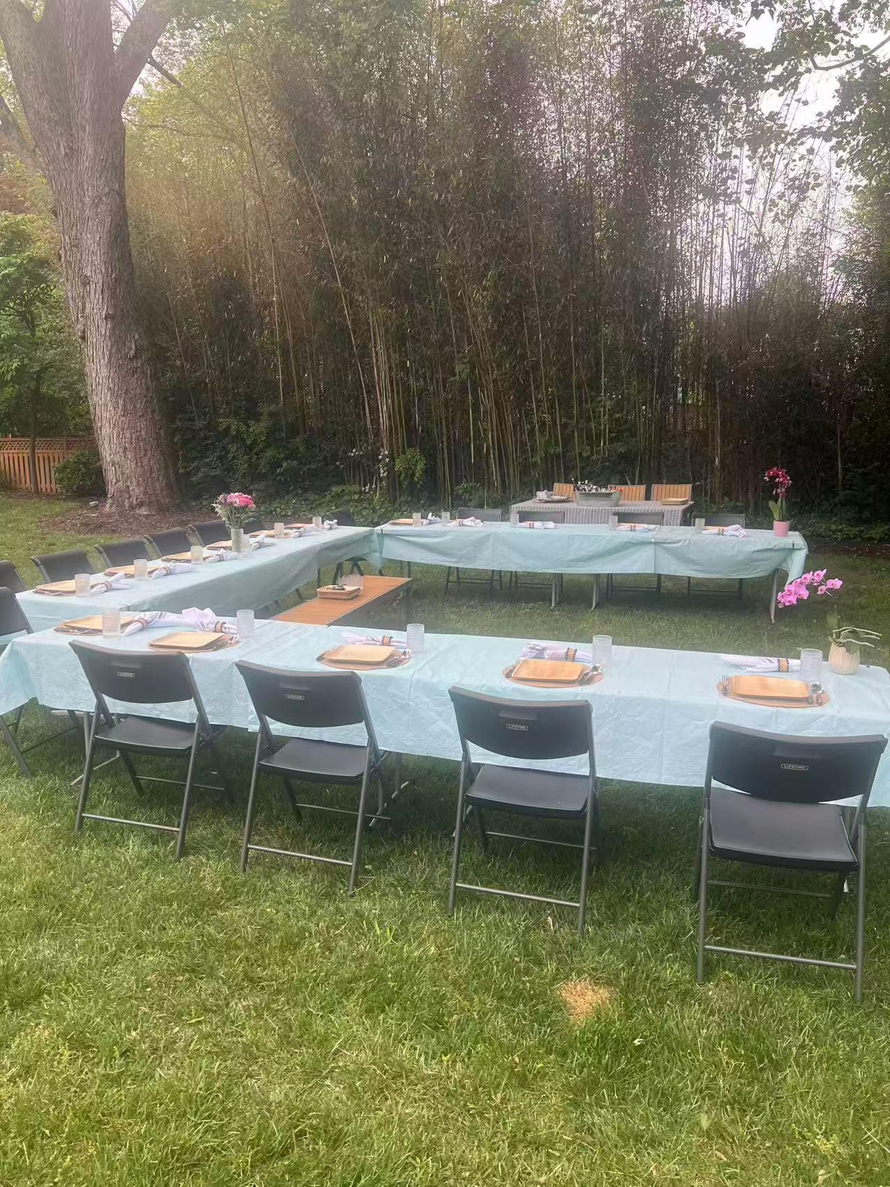 Backyard event setup with light blue tablecloths, bamboo, and large tree