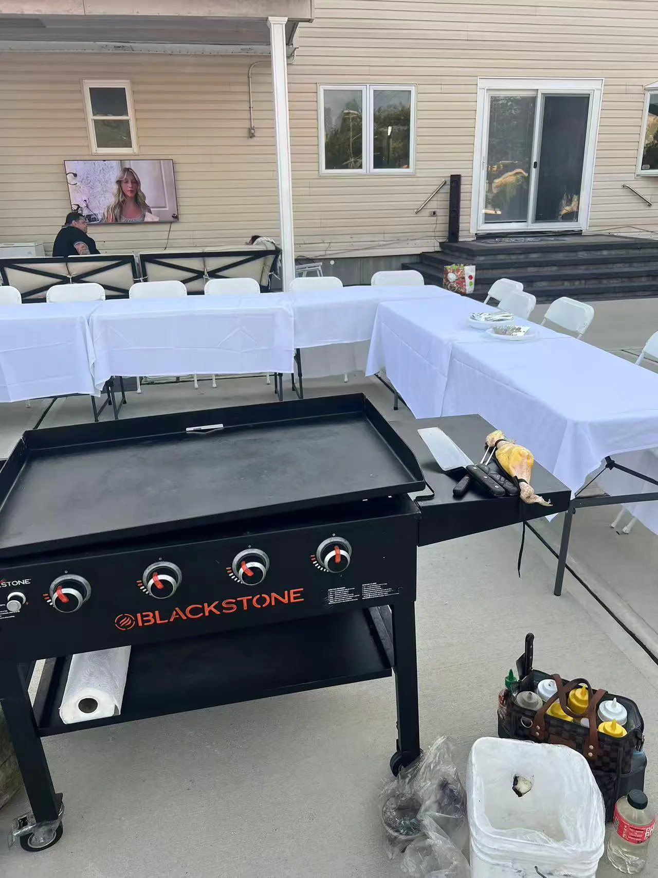 Blackstone griddle on patio with event tables, TV, and cooking tools